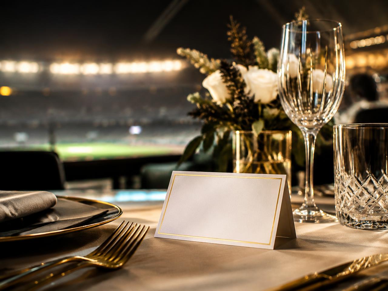 Hospitality table with a blank gold-edged place card and stadium lights beyond